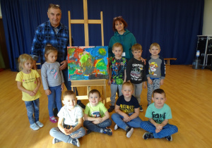 10 wspólne zdjęcie Krasnali, dzieci stoją i siedzą wokół obrazu, przy obrazie stoi pan Lesław i pani Ewa